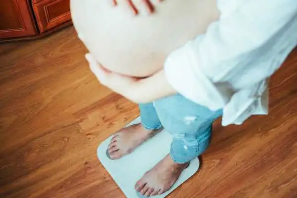 Image of woman weighing herself and experiencing weight gain through pregnancy Purfleet
